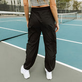 Rear view of black Jetsetter Cargo Joggers showcasing an elastic waistband and cargo pockets on a pickleball court