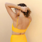 Back view of the yellow Rise Bikini Top in Golden Terry showcasing thin straps and a wide band on a model