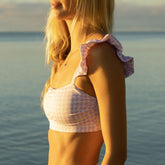 Side view of lavender houndstooth Bella crop top showcasing ruffled shoulder straps with water in background