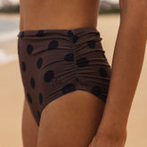 Rear close-up of Black Cocoa Dot Ruched Midi Bottoms showcasing ruched center seam and dot pattern against sandy background