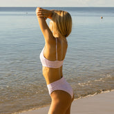 Rear three-quarter view of lavender houndstooth Almost Cheeky Midi Bottoms on a model at the beach