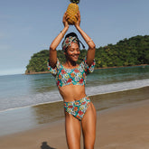 Model holding a pineapple on a beach wearing teal floral Costa Almost Cheeky bikini bottoms