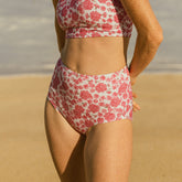Rear view of Athena High-Waisted Bottoms showcasing pink floral print and full coverage fit on a model at the beach