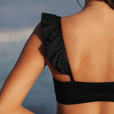 Close-up back view of the Black Bella Crop Top showcasing a ruched strap and wide band against a blue-gray background
