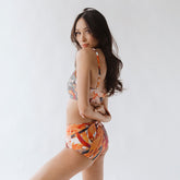 Rear view of Pixie High-Waisted Bottoms showcasing orange abstract pattern and high-waisted fit on model with white background