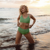 Front view of green high-waisted bottoms showcasing the fit on a model in shallow ocean water