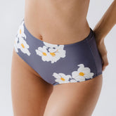 Close-up front view of Daisy High-Waisted Bottoms showcasing white and yellow floral print on slate blue fabric worn by a model against a white background