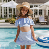 Young girl in a blue and white striped swimsuit and hat by a pool.
