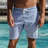 Front view of Wind and Sea Shorts in Sand Bar Blue with blue-and-white stripes, drawstring waist, and side pockets by a pool