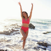 Front view of the pink gingham Rise Bikini Top showcasing its scoop neckline on a model at a rocky beach
