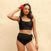 Front view of Black Olivia Swim Crop showcasing its scoop neckline and wide straps on a model against a peach stucco wall