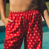 Close-up of red Slip On Trouser, Star showcasing a white star pattern and elastic waistband with a poolside background