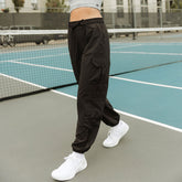 Side view of black Jetsetter Cargo Joggers worn by a model, showcasing cargo pockets and elastic cuffs on a tennis court