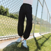 Three-quarter view of black Jetsetter Cargo Joggers showcasing cargo pockets and elastic cuffs on a model by a chain-link fence