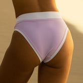 Rear view of Bleacher Almost Cheeky Midi Bottoms in lavender showcasing white trim on a model with a warm neutral background
