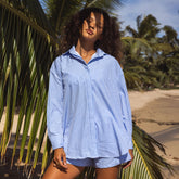 Front view of the loose-fitting Kimber Button Down in Sand Bar Blue with blue and white stripes on a model at a tropical beach