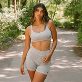 Front view of the fitted heather grey Momentum Bra with scoop neckline and wide straps, worn on a wooded path