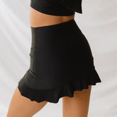 Side view of black high-waisted swim skirt showcasing a flared ruffle hem on a model against a white background