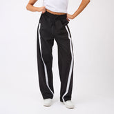 Front view of black Sideline Track Pants showcasing white dotted side stripes and drawstring waist, worn by a model