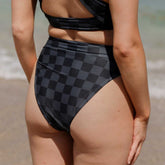 Rear view of Slate Check Almost Cheeky Bottoms showing a slate check pattern and high waist on a model at the beach